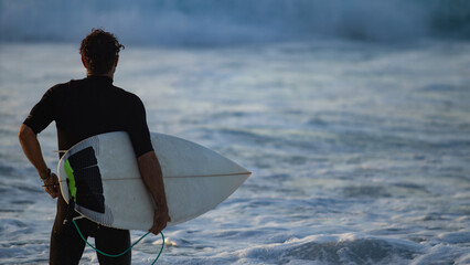 Surfer looking at the ocean ready to hit the perfect wave thanks to his surfboard. We are in...
