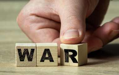 The inscription WAR on wooden blocks with a finger turning the blocks. Wooden Cubes war, Cubes with war