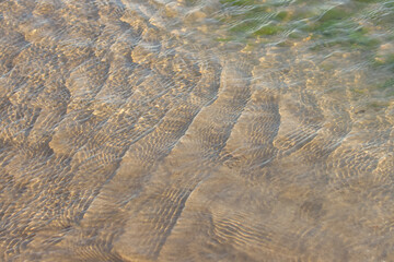 Clear, transparent, ripple ocean water over beach sand.