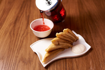 pancakes with sour cream and black tea on a wooden background