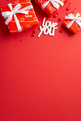Saint Valentine's Day concept. Top view vertical photo of red present boxes with white ribbon bows inscription love you and sprinkles on isolated red background with empty space
