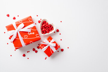 Valentine's Day concept. Top view photo of red gift boxes with ribbon bows and heart shaped saucer with sprinkles on isolated white background
