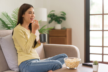 Concept of activity in home, Young woman is drinking coffee and eating popcorn while watching tv