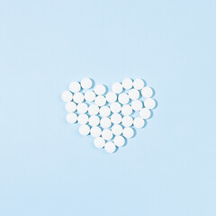 Heart shape of white pills with red heart inside on light blue background in hard light with shadow, top view, copy space, square. Medical, treatment background - remedies for prevent and therapy.