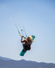 Female kitesurfer in full jump performing an artistic and extreme figure with her board above the water of the Mediterranean Sea in Corsica near Propriano 