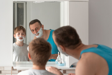 Obraz premium Dad and son in shaving foam on faces have fun in bathroom. Morning facial hygiene