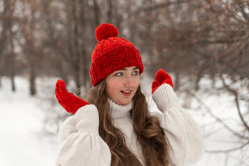 Portrait of happy beautiful young woman in knitted red hat and mittens and woolen sweater in winter...