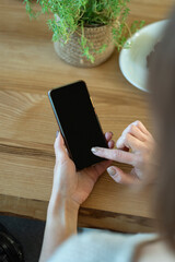 Telephone in women hands against on wooden table background. Smartphone with blank black screen. Vertical frame.