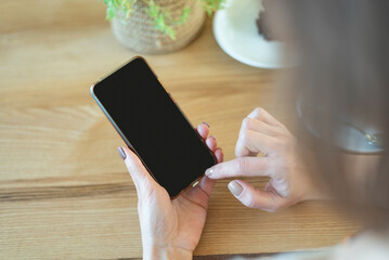 Woman hands with smart phone, blank black screen. View over shoulder. Woman in cafe during breakfast