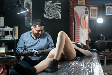 A tattoo artist is smiling while talking with his woman client during a tattoo session