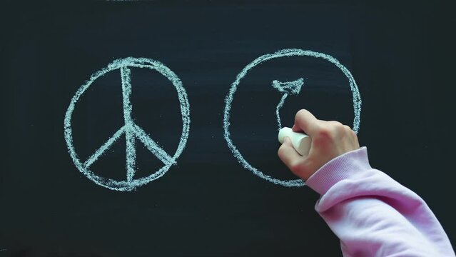 Timelapse, The close-up of a child's hand drawing with chalk on a blackboard a sign of pacifica and peace and a crossed-out bomb. Anti-war protest concept