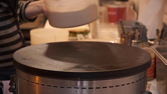 Making crepes outoors on a metal griddle with wooden stick. Close-up of vendor man cooking crepe in Paris street. The concept of delicious fast food-Dan. Pancakes
