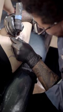 A tattoo artist is tattooing a snake on a woman's leg. Close up.