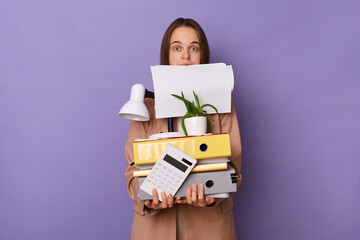 Portrait of busy funny woman with papers in mouth wearing beige jacket holding lot of documents...