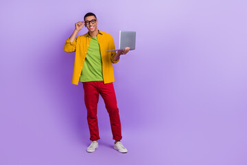 Full length photo of handsome guy arm touch eyeglasses hold netbook empty space isolated on violet color background
