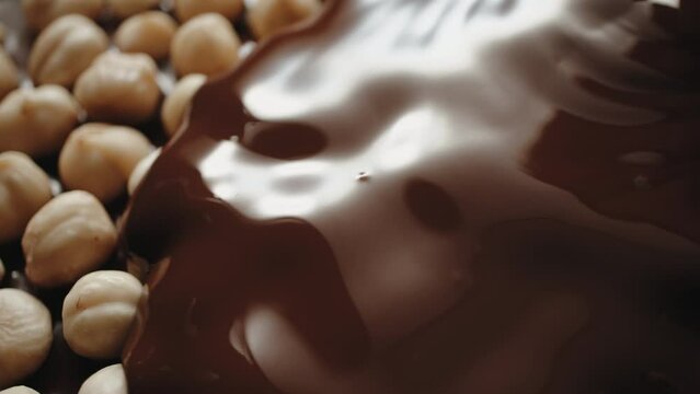 Close-up whole hazelnuts pouring with hot melted chocolate, flowing molten milk chocolate or brown caramel sauce and nuts. Cooking chocolate bar, dessert, candies. Confectionery manufacture