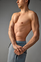 Side view photo of muscular, strong, relief male body. Cropped portrait of mature man posing shirtless over grey studio background. Men's health and beauty