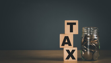 Wooden tiered cubes with the text TAX and a glass jar with coins inside on a wooden table. ,Personal income tax concept,Financial planning,Income management to pay personal taxes