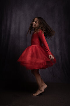 happy girl in red dress dancing in studio on bare feet in dark painterl style