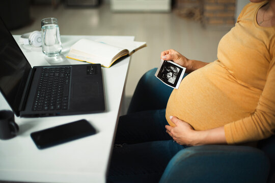 Beautiful young pregnant woman looking at ultrasound pictures of her baby. Businesswoman in office..