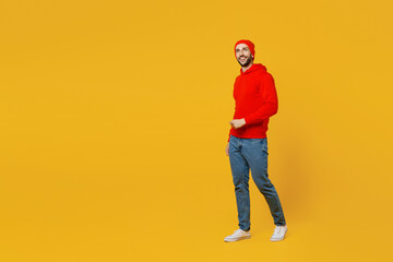 Fototapeta na wymiar Full body side view smiling happy fun young caucasian man wears red hoody hat look camera walking going strolling isolated on plain yellow color background studio portrait. People lifestyle concept.