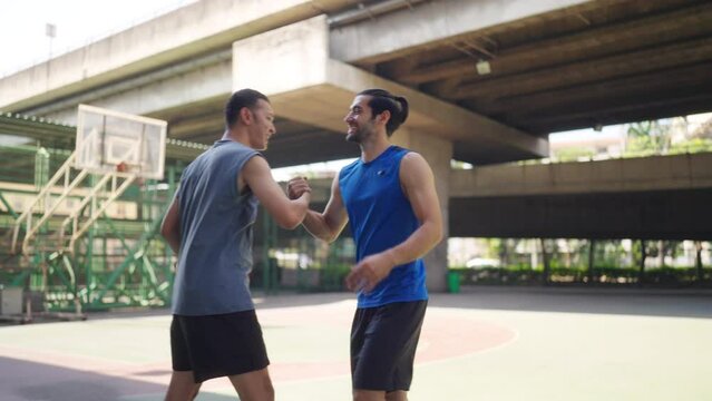 Two man basketball players shaking hand after playing one on one streetball match together on outdoors court under highway in the city. Fair game sport competition and outdoor sport training concept.