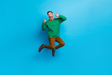 Fototapeta na wymiar Full size photo of mature attractive male jumping high showing double thumb up wear trendy green clothes isolated on blue color background