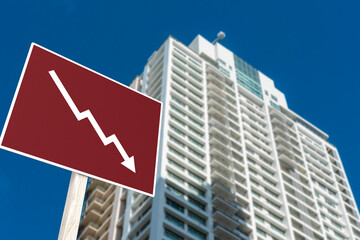 A sign showing an downward arrow in front of a highrise condominium or apartment. Concept of...