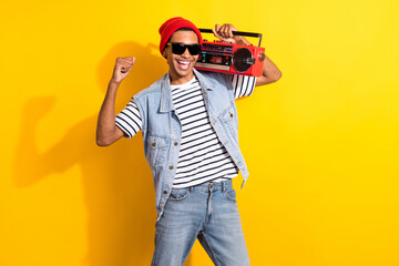 Portrait of overjoyed delighted carefree handsome guy have fun raise fist hold boombox isolated on yellow color background