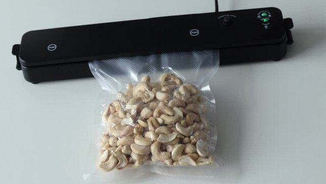 Vacuum packaging machine packs and seals nuts in vacuum packs Device for packing food and sucking air on a white table with a plastic cashew bag.