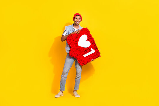 Full length photo of cute sweet guy dressed denim clothes holding heart like pinata isolated yellow color background