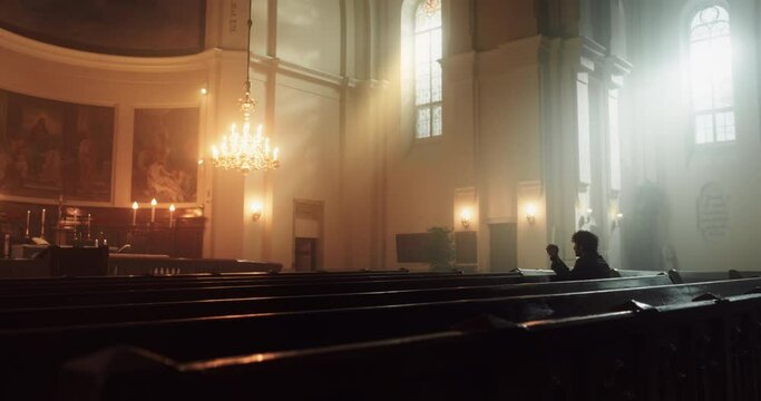 A Devout Christian Sits Piously In A Grand Church, Folding Hands for Praying, Contemplating Their Earthly Life. Parisher Seeks Moral Guidance From the Faith. Religious Atmosphere Of The Sacred Space