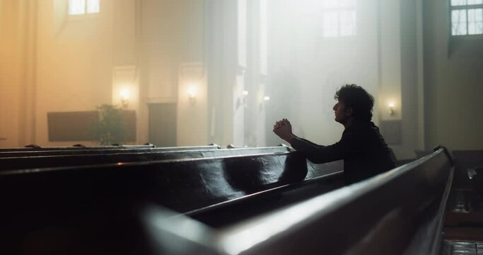 Young Christian Man Sits Piously in Majestic Church, with Folded Hands He Seeks Guidance From Faith and Spirituality while Praying. Religious Belief in Power and Love of God. Slow Motion Side View