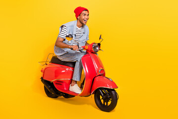 Full length photo of cute excited man wear jeans outfit riding moped looking empty space isolated yellow color background