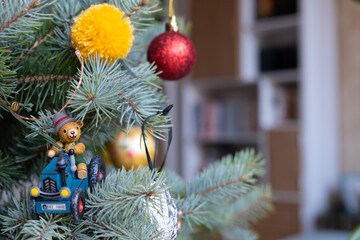 Christmas tree background: close-up of traditional nostalgic vintage wooden decoration (bear on a tractor) on blue spruce in a living room with copy space