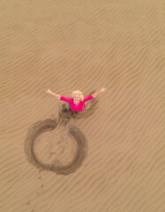 Caucasian white woman relaxing in the dunes. Maspalomas dunes in Gran Canaria, view from above. Woman looking up in the dunes. Drone photography