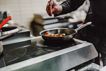 man chef cooking tasty shrimp in frying pan on kitchen