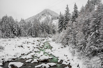 Mountain river through snowy mountains during winter snow fall