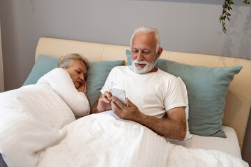 Senior man using smart phone in bedroom