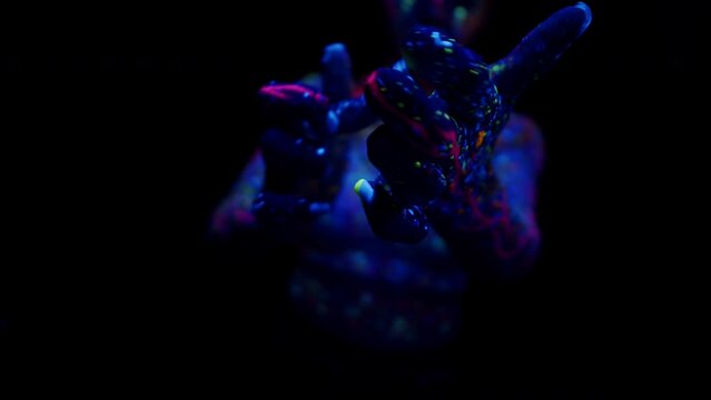 Close-up young artistic modern woman, flexible girl dancer dancing black studio background in fluorescent Neon UF Light. Art, motion, flexibility, inspiration concept. Flexible artist. Beauty of woman