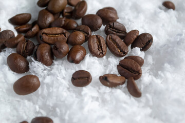 Coffee beans in the snow. Coffee contrasts with white snow. Coffee beans are scattered on the white...