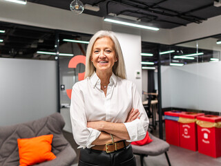 Cheerful aged female entrepreneur standing in office