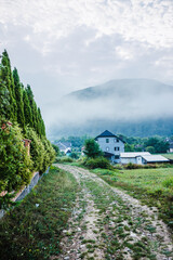 Fototapeta na wymiar Mountain from view with small village and flow fog. Foggy summer morning in the mountains and a small village. Country road in the mountains. Carpathians. Polyana. Ukraine