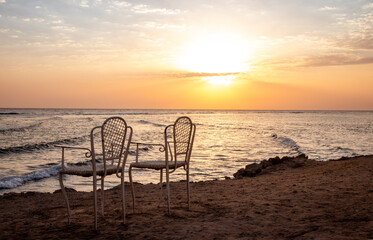 Fototapeta na wymiar Beautiful sunrise at sea from the ledge to meet the dawn. Dawn on the Red Sea. The sun is reflected in the sea. Light clouds in the blue dawn sky. Beautiful chairs by the sea. Tropical sunrise