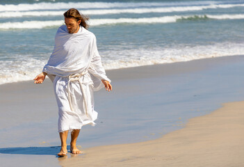 Man with white robe and beard walks on the beach