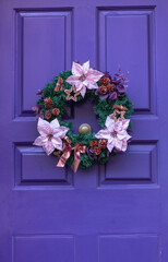 Fototapeta na wymiar Christmas wreath with bright flowers on door of purple color