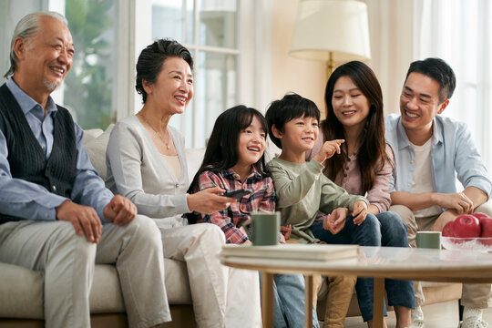 three generation asian family watching tv together at home