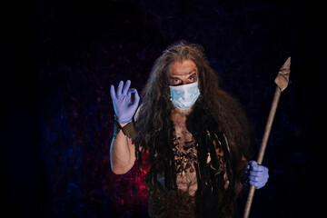 Primitive man with long hair and a beard in a medical mask and gloves on a dark background