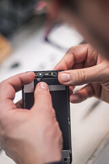 In the electronics repair shop, the master repairs, cleans, controls, arranges the smartphone. Uses equipment and tools for work. Workplace top view, close-up.
