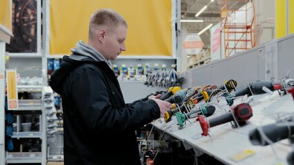 A man in a hardware store chooses electrical goods. The buyer in the store chooses a screwdriver. Buying a screwdriver at a hardware store. Cordless Power Tools